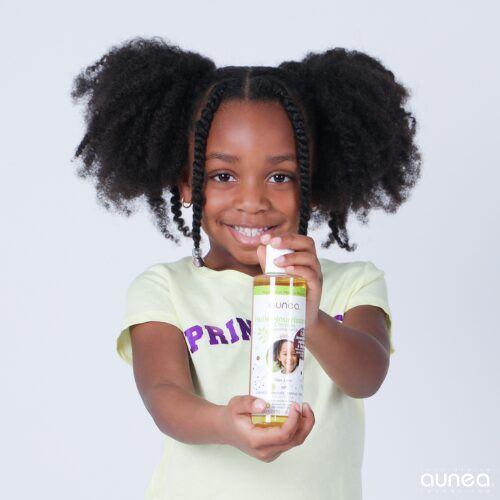 Une fille noire souriante aux cheveux naturels tient une bouteille d'huile capillaire.