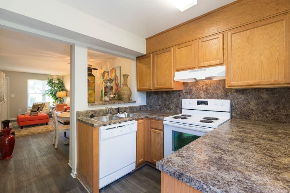 A kitchen with wooden cabinets , a stove , dishwasher , and granite counter tops at Old Mill Townhomes in Lynchburg, VA.