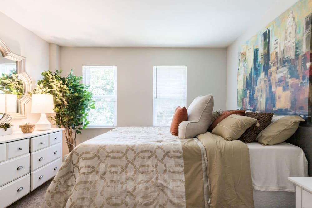 A bedroom with a bed , dresser , mirror and painting on the wall at Old Mill Townhomes in Lynchburg, VA.