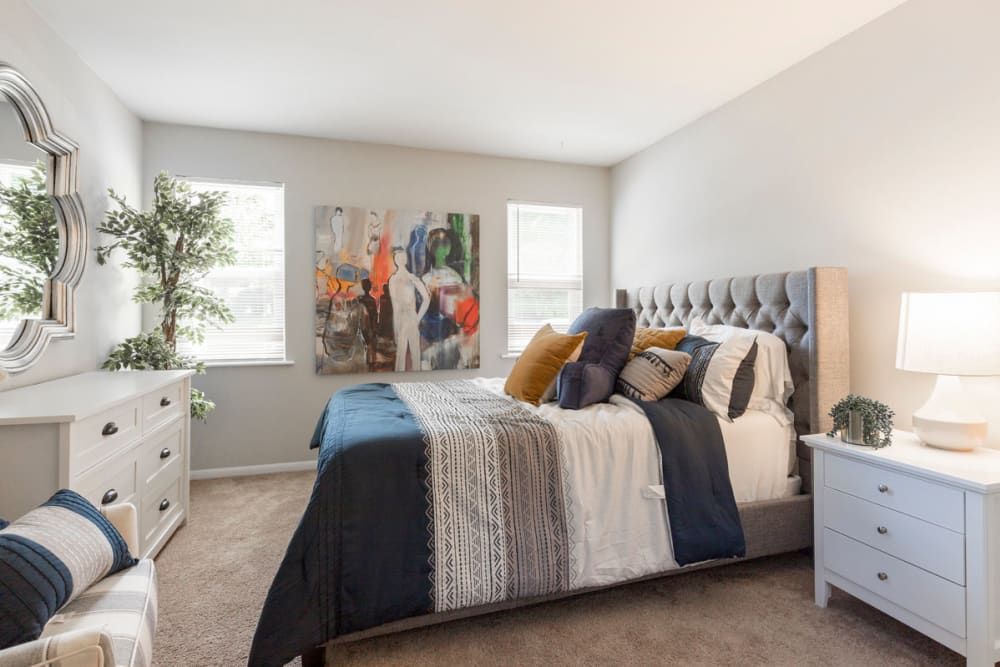 A bedroom with a bed , dresser , nightstand , mirror and painting on the wall at Old Mill Townhomes in Lynchburg, VA.