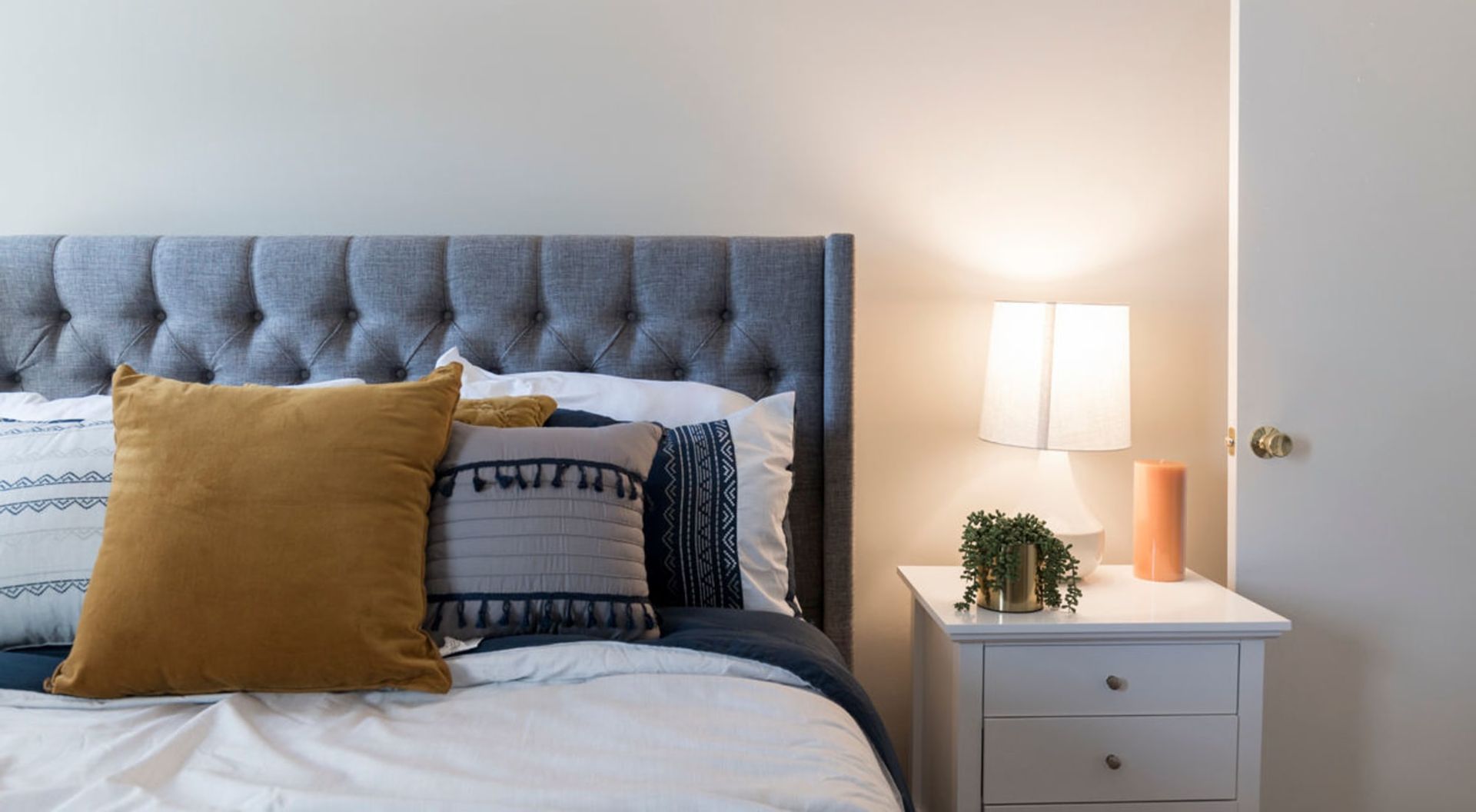 A bedroom with a bed , nightstand , lamp and door at Old Mill Townhomes in Lynchburg, VA.