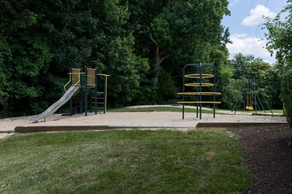 A playground with a slide and swings in a park surrounded by trees at Old Mill Townhomes in Lynchburg, VA.