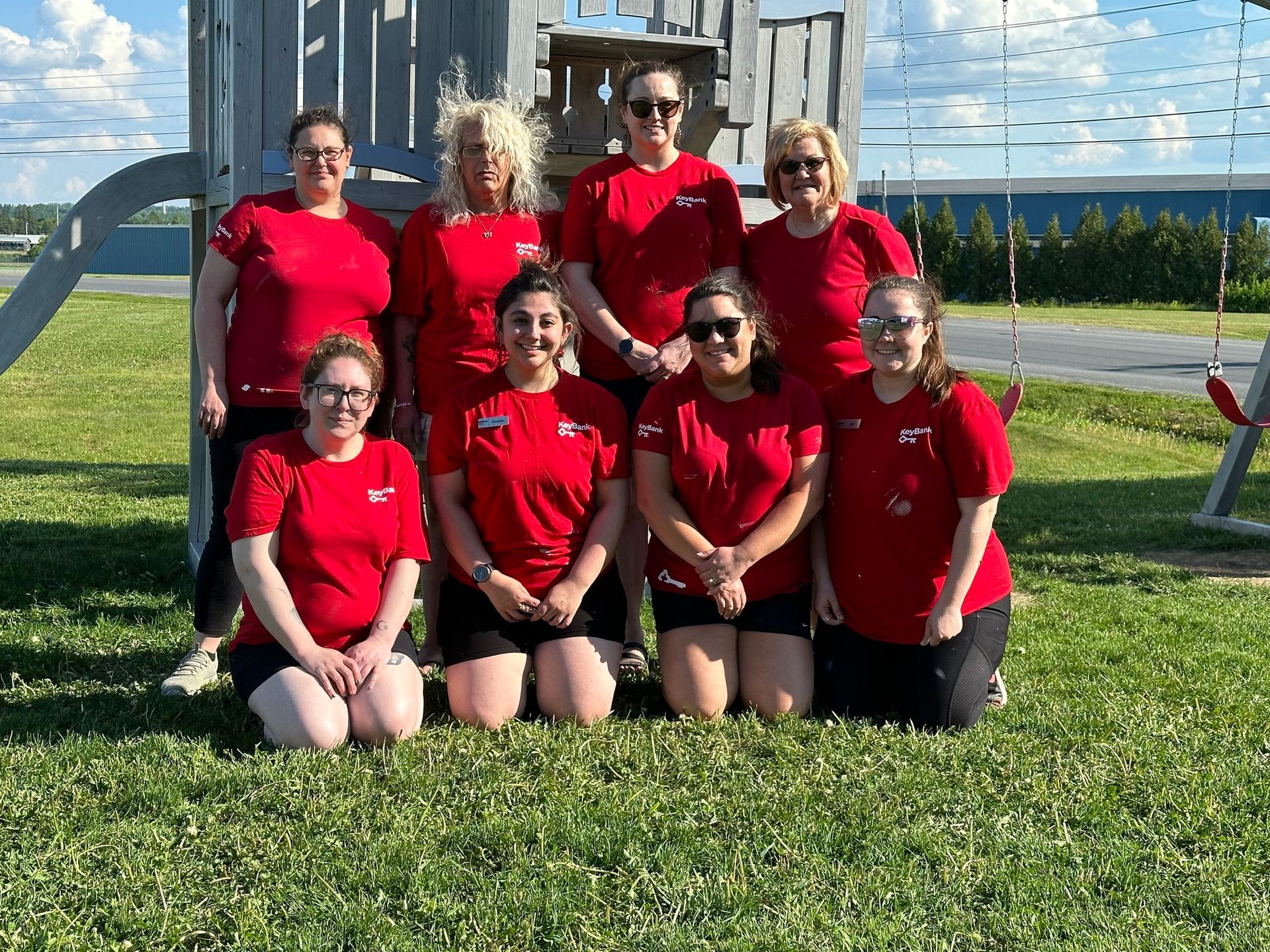 A group of people wearing matching black jackets stand on a gravel surface near the back of an open school bus.