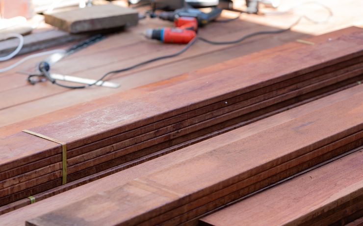 A work in progress at a Salinas deck building site, with a stack of reddish-brown hardwood decking planks and construction tools in the background.