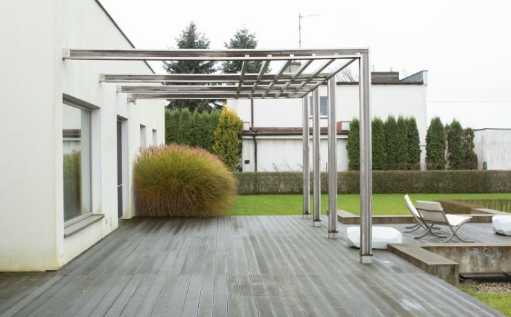 Modern home with a sleek aluminum pergola over a gray composite deck in a Salinas backyard, featuring minimalist outdoor furniture and vibrant green landscaping.
