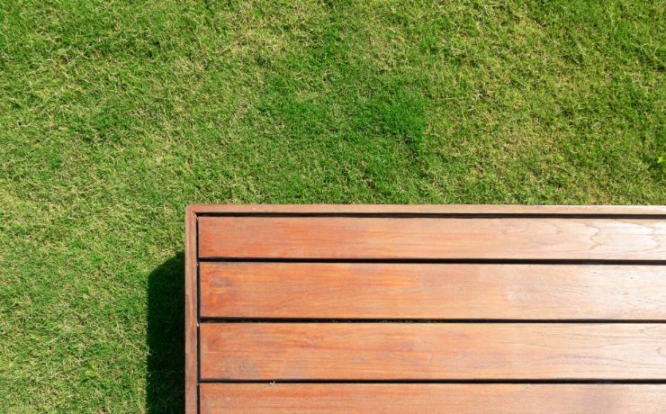 The edge of a richly stained wooden deck in Salinas, neatly abutting a well-manicured lawn, showcasing precise construction and care.