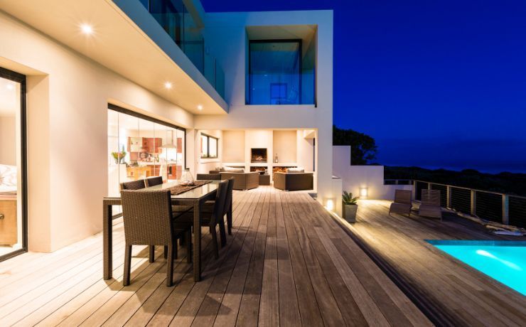 Luxurious Salinas evening on a spacious wooden deck featuring an outdoor kitchen and dining area, with ambient lighting and a pool reflecting the night sky.