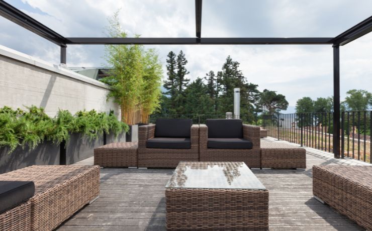 Chic rooftop wooden patio in Salinas with modern rattan furniture under a black metal pergola, complemented by greenery and a view of the city skyline.