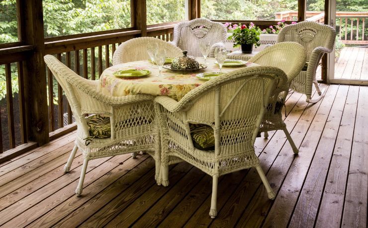 A charming white wicker dining set on an aged wooden deck surrounded by lush greenery in a Salinas home, inviting outdoor enjoyment.