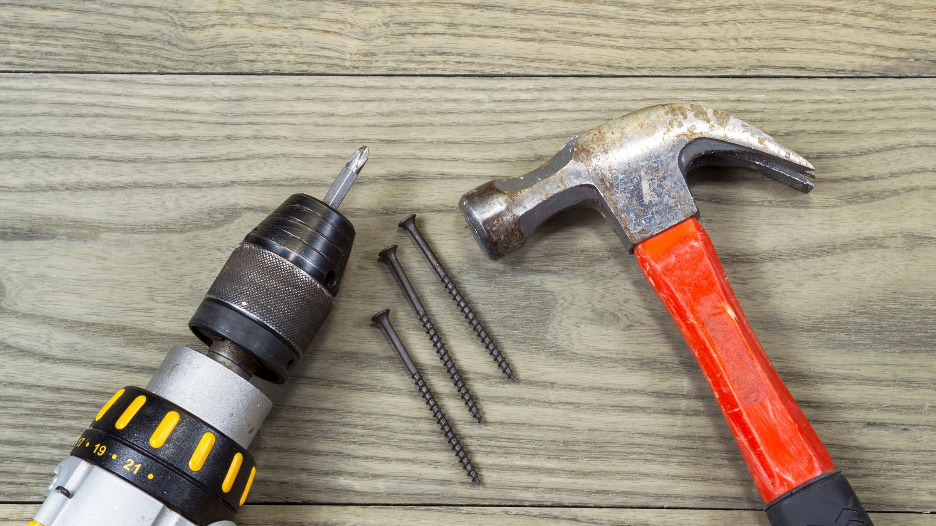 Tools for deck building: a drill, hammer, and nails on wood.