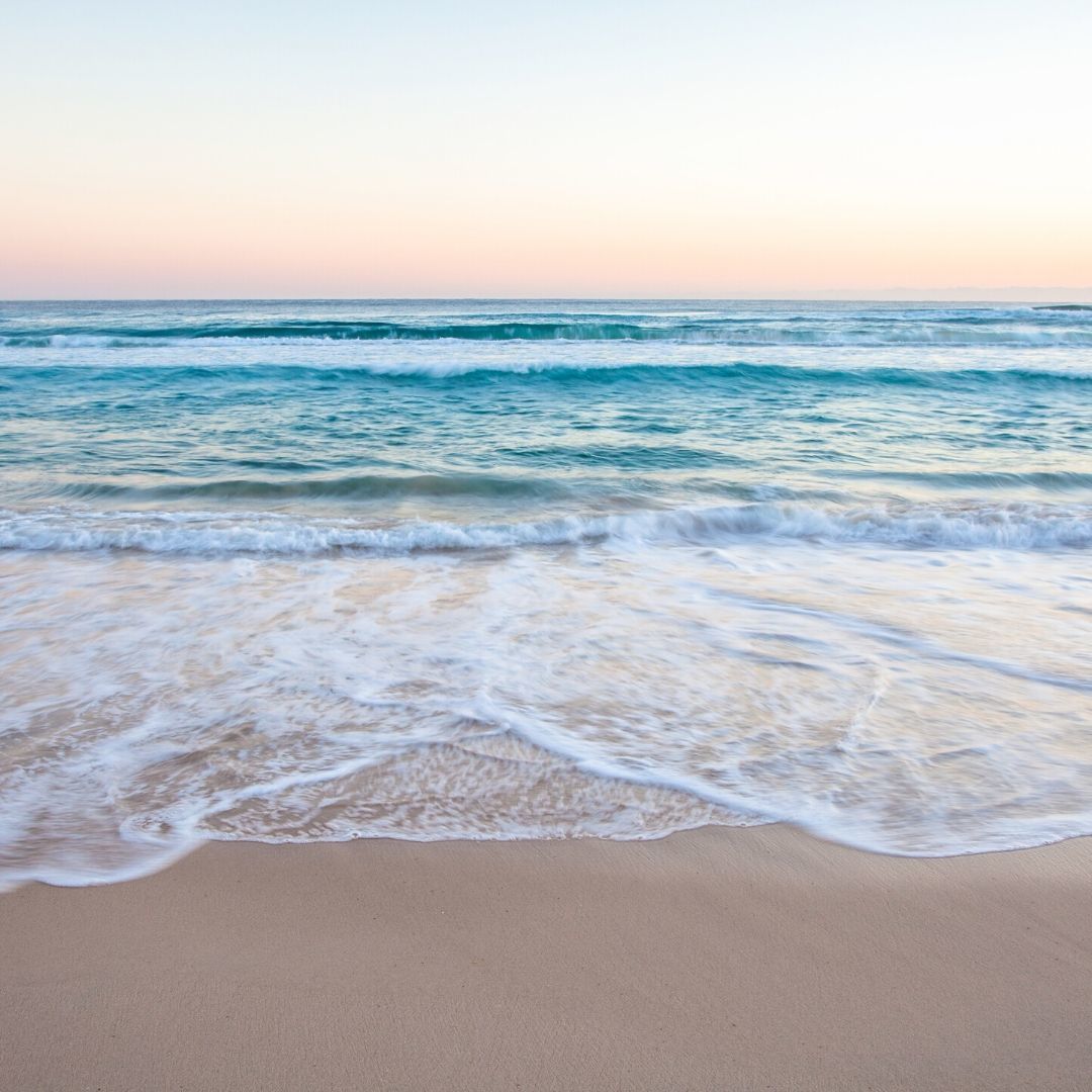 A sandy beach with waves crashing on the shore at sunset.