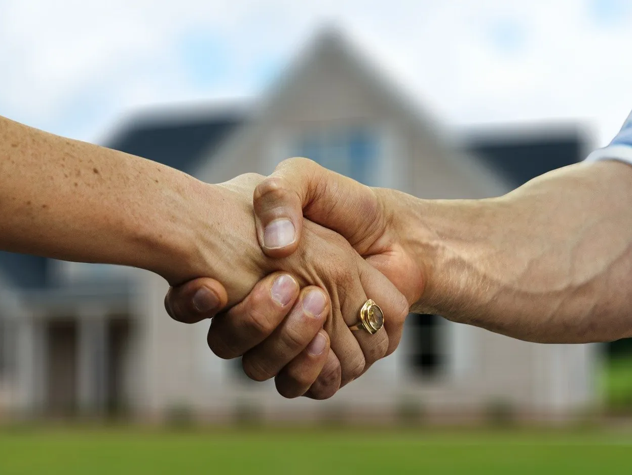 A man and a woman are shaking hands in front of a house.