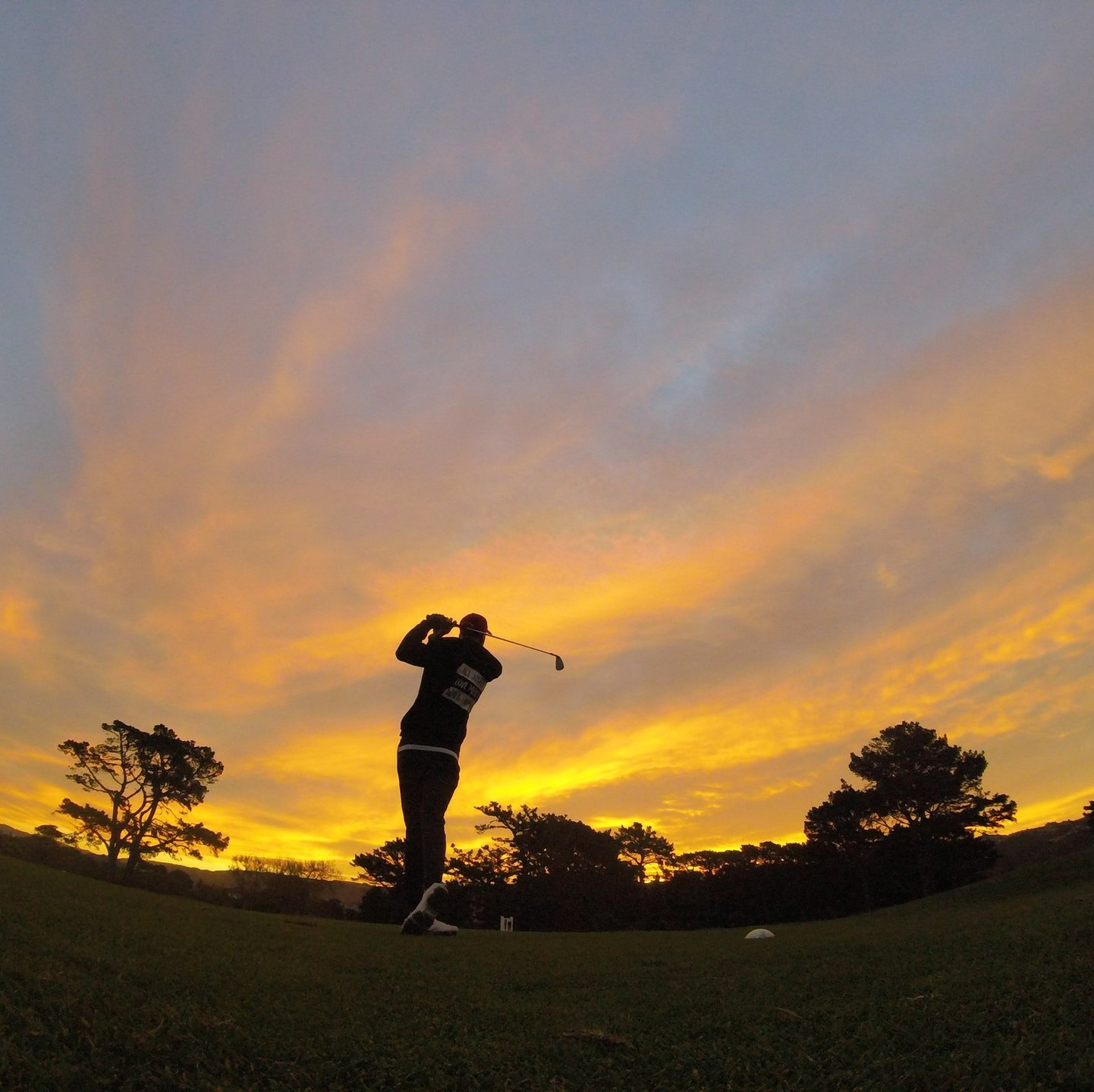 A man is swinging a golf club at sunset