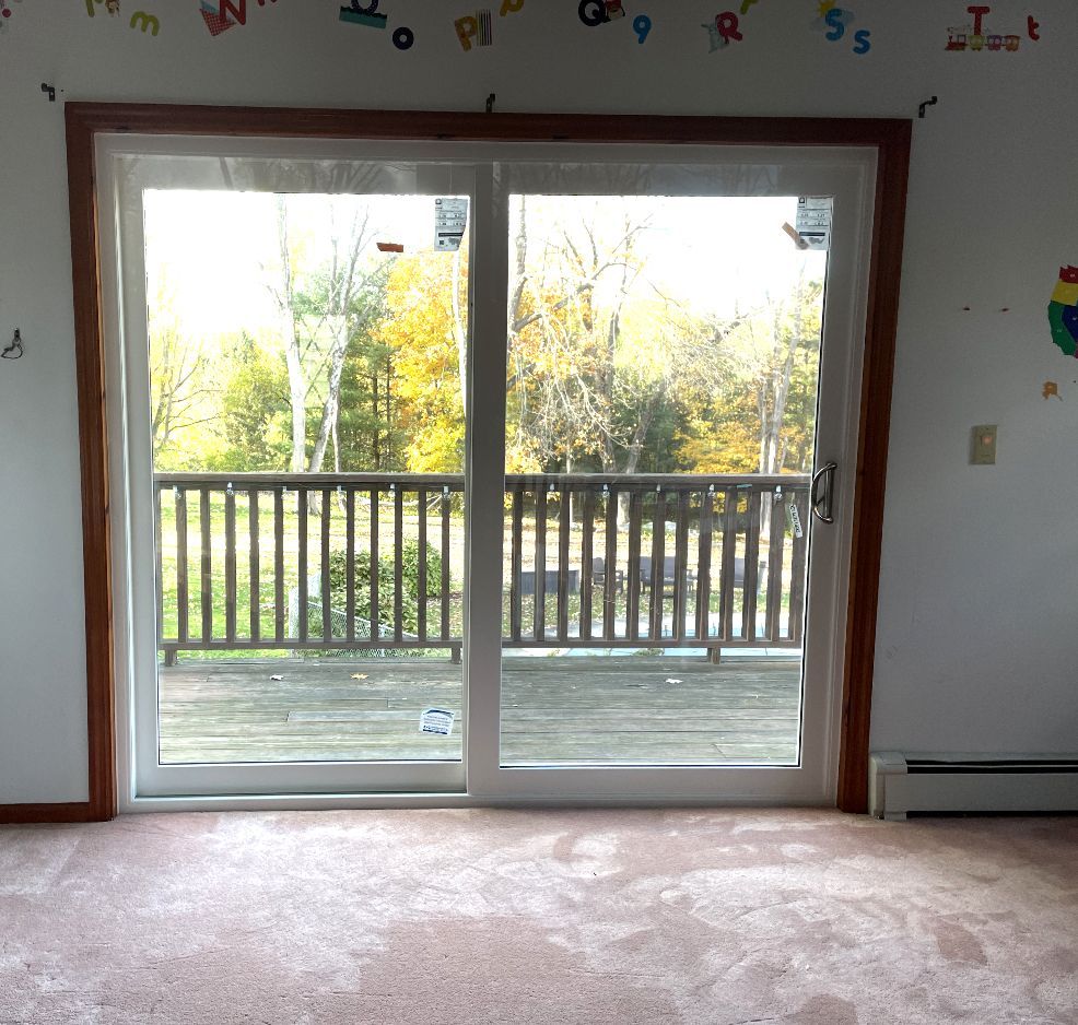Sliding glass door leading to a wooden deck surrounded by trees.