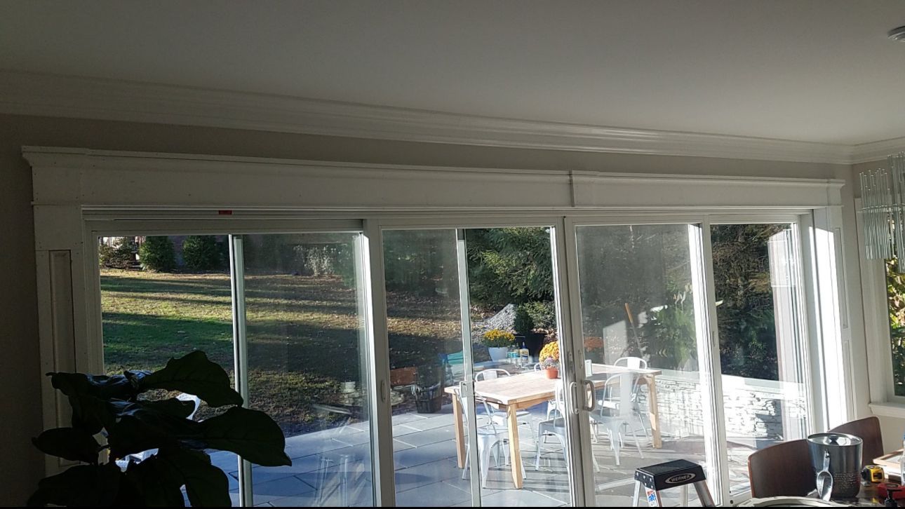 Large glass windows with white trim, view of green lawn, and patio with table and chairs.