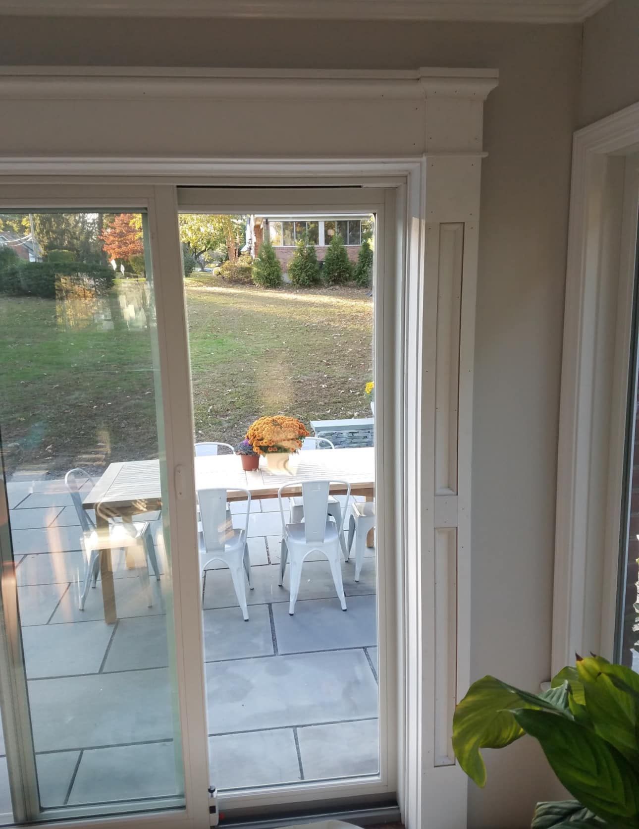 Sliding glass door frames outdoor dining table and chairs on a stone patio, visible from inside a room.