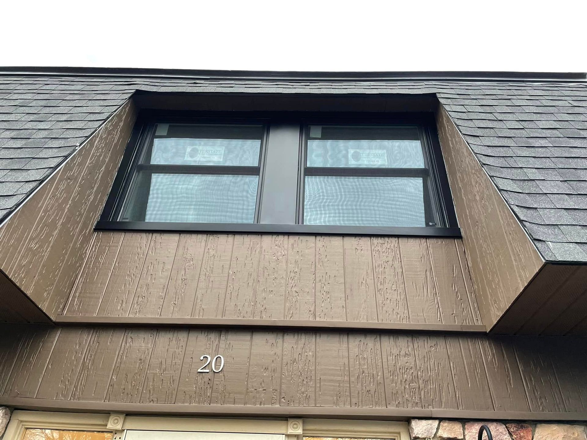 Brown house with dark roof and two windows. Number 20 below windows.