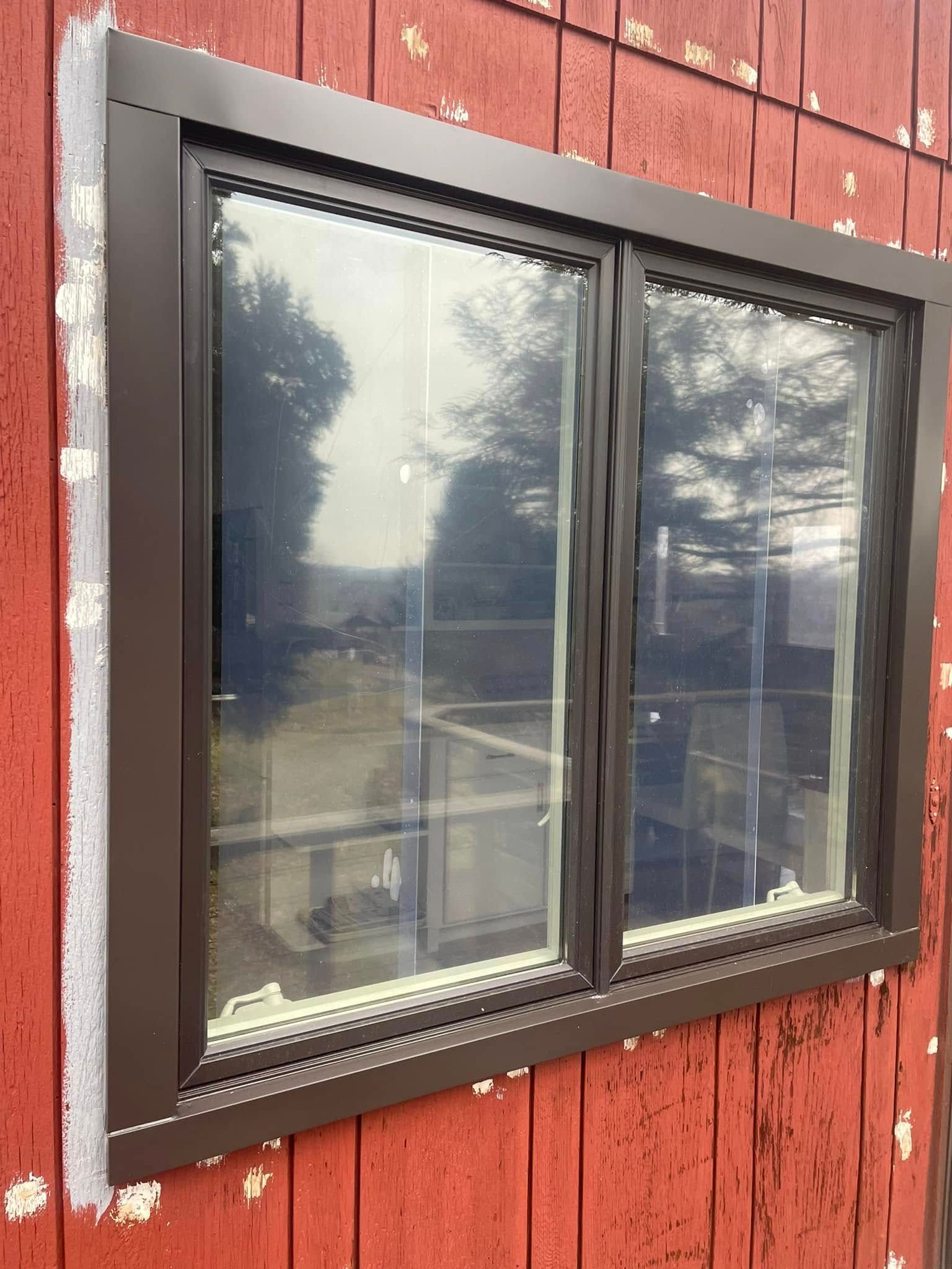 Brown-framed double-pane window installed on a red wooden wall. The window reflects a blurred outdoor scene.