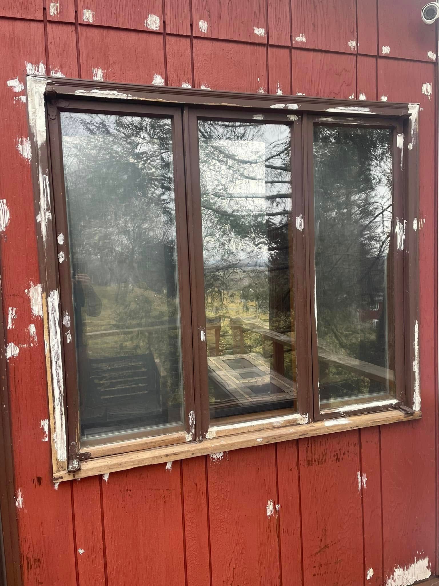 Window with brown frames in red weathered building, peeling paint.