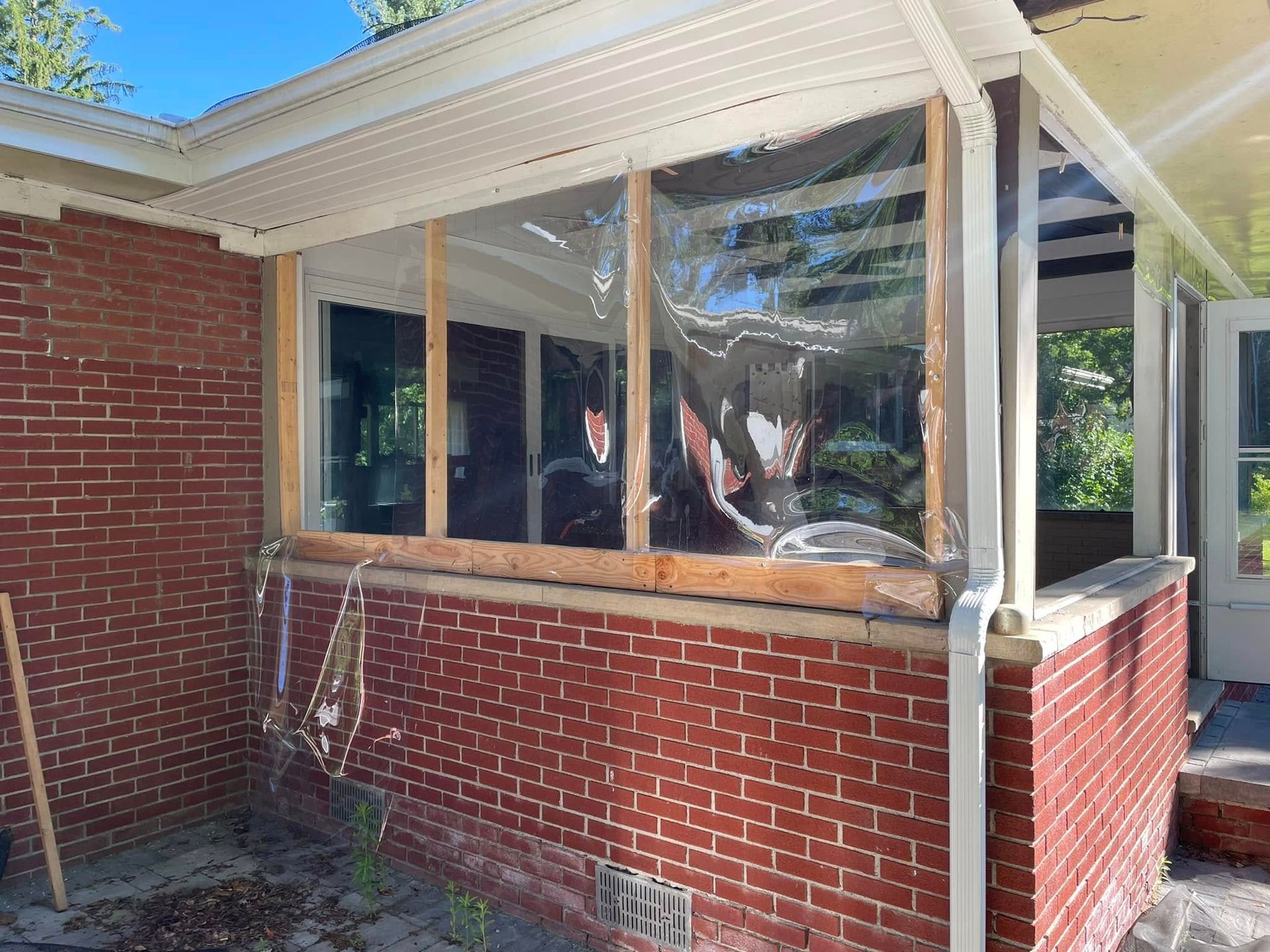 Brick building exterior with clear plastic sheeting on a porch, wooden framing.