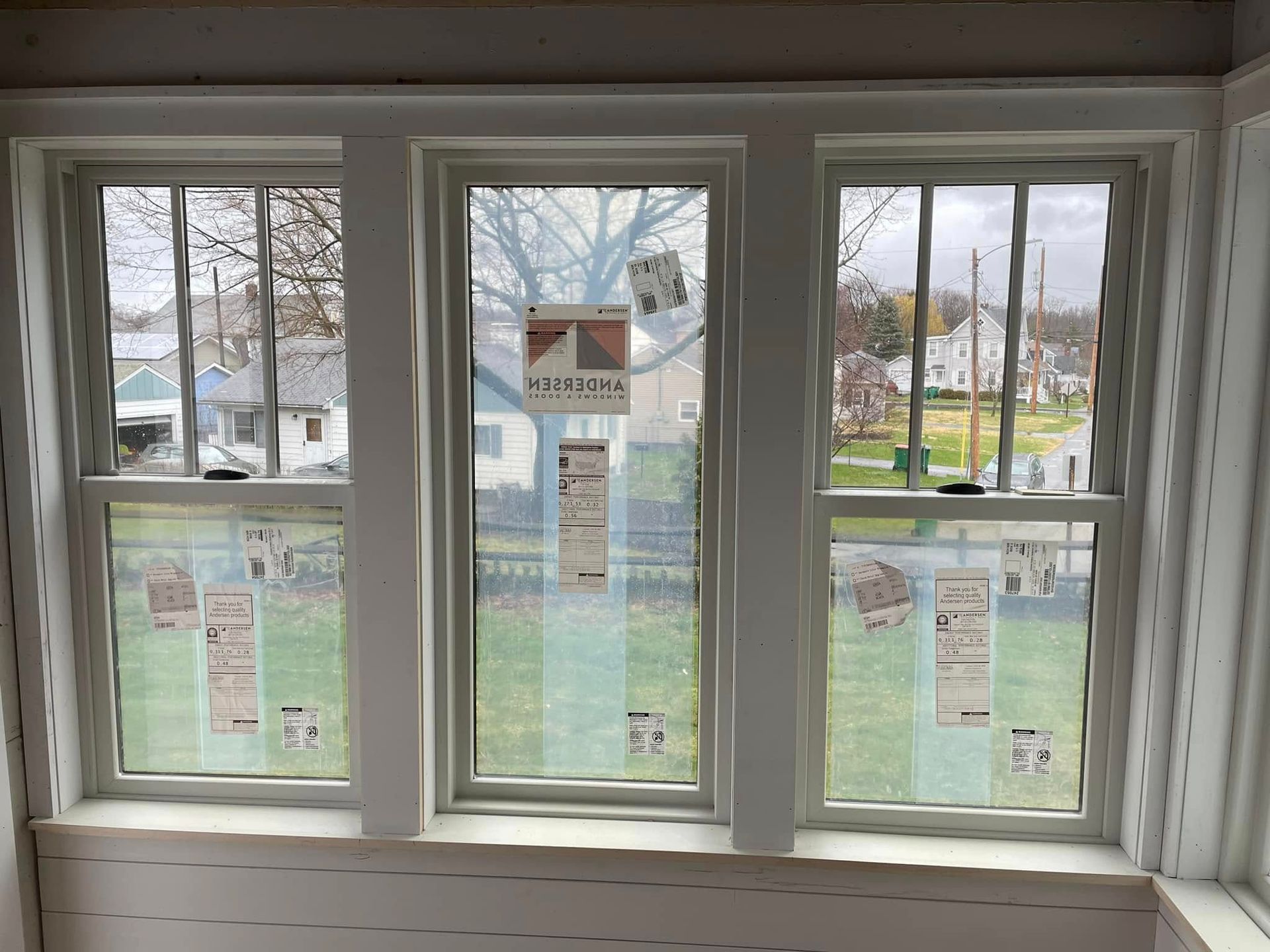 Three vertical windows with white trim, looking out onto a residential street. Some stickers are on the windows.
