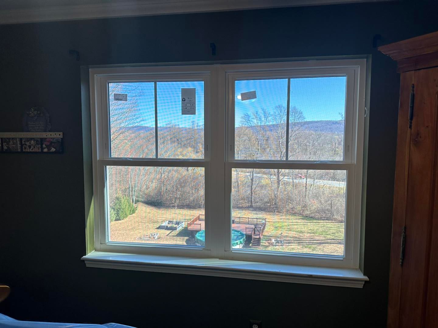 Double-hung window looking out onto a rural landscape with mountains. The window frames are the interior wall is dark green.
