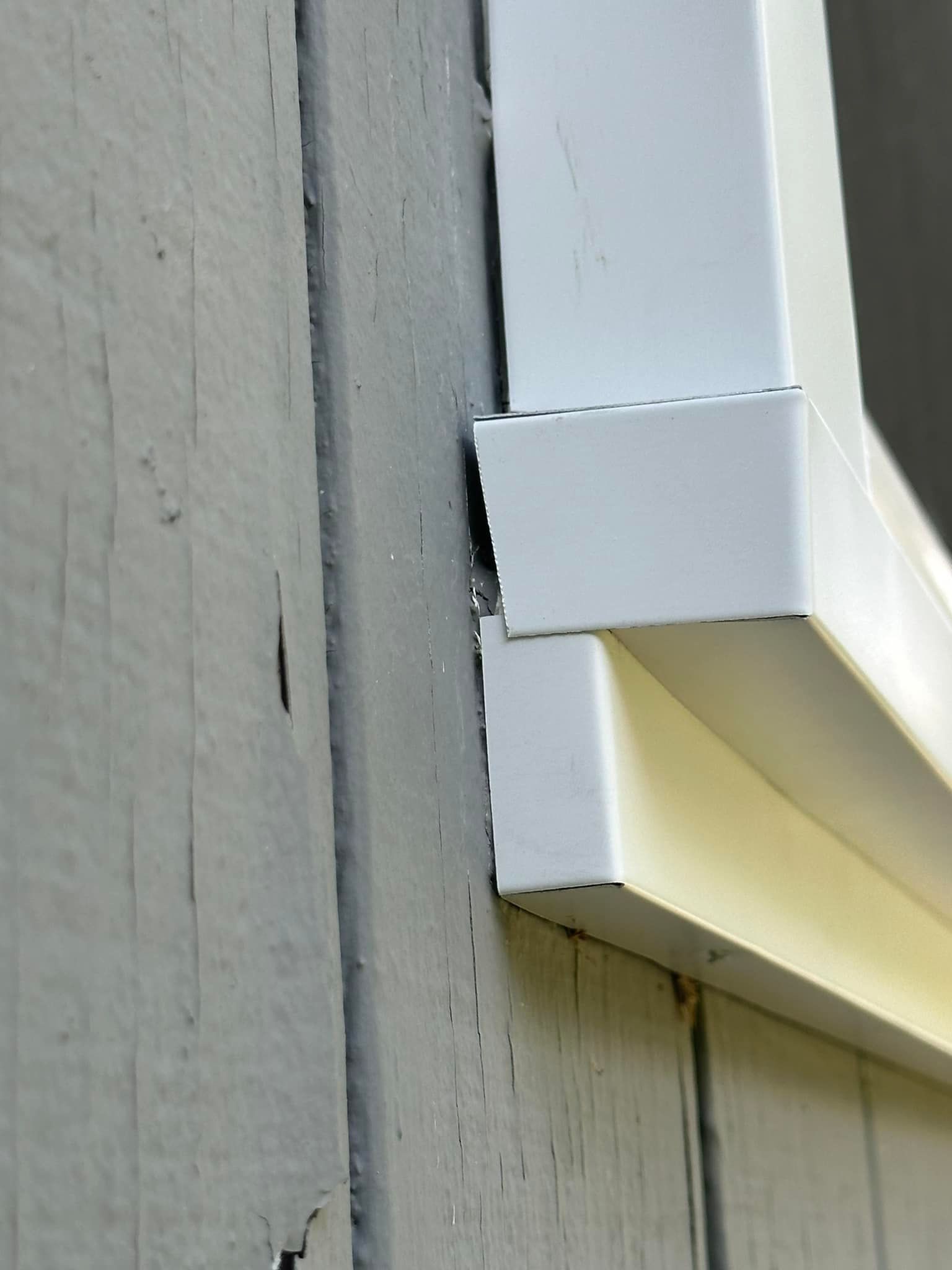 White window trim with a slight gap against grey, weathered siding.
