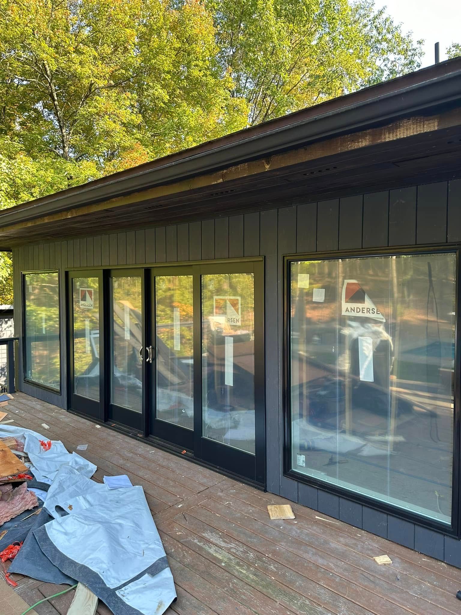 Exterior view of a building with dark gray siding, large windows, and a wooden deck.
