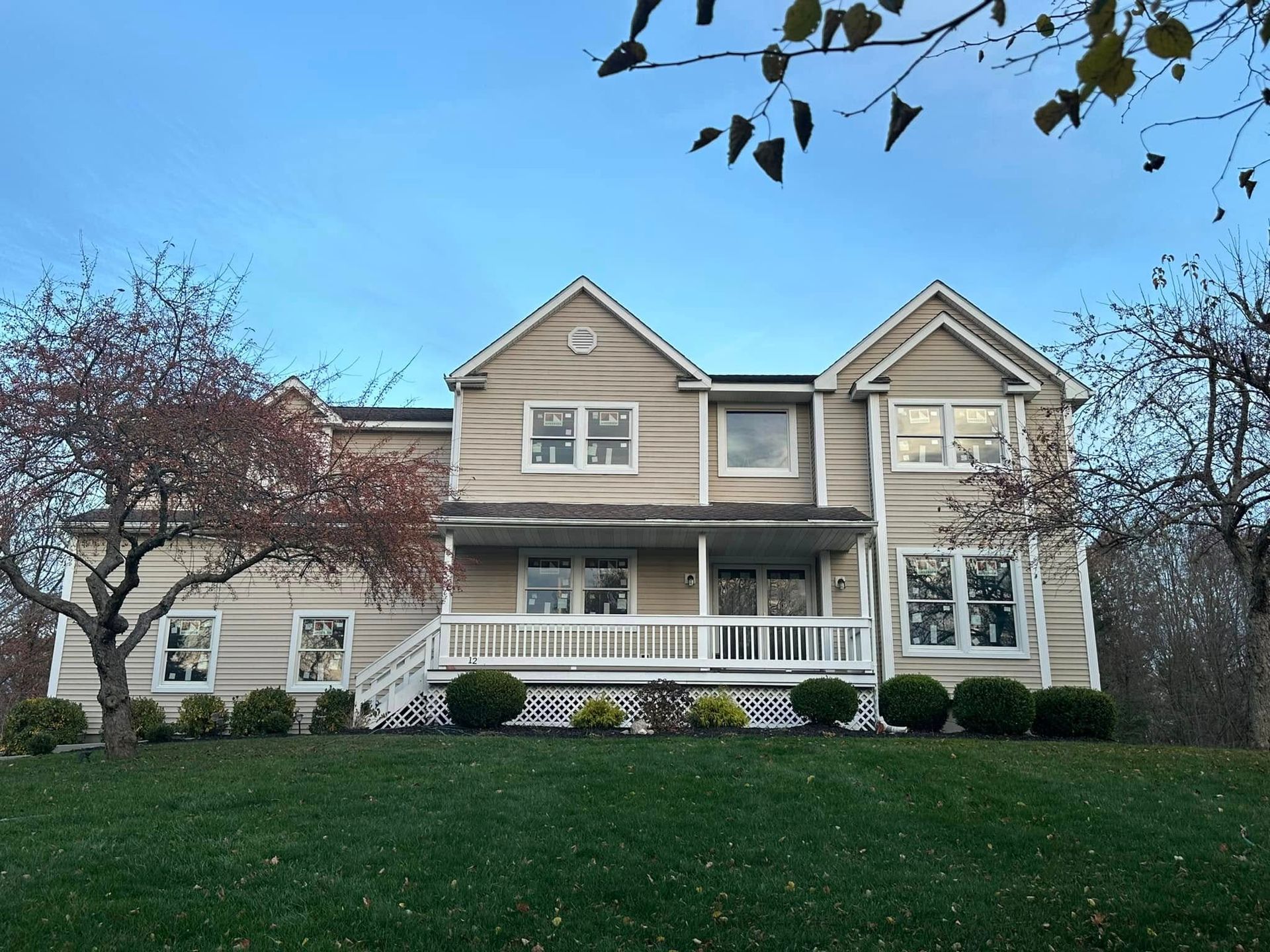 Two-story beige house with white trim, porch, and a grassy yard under a blue sky.