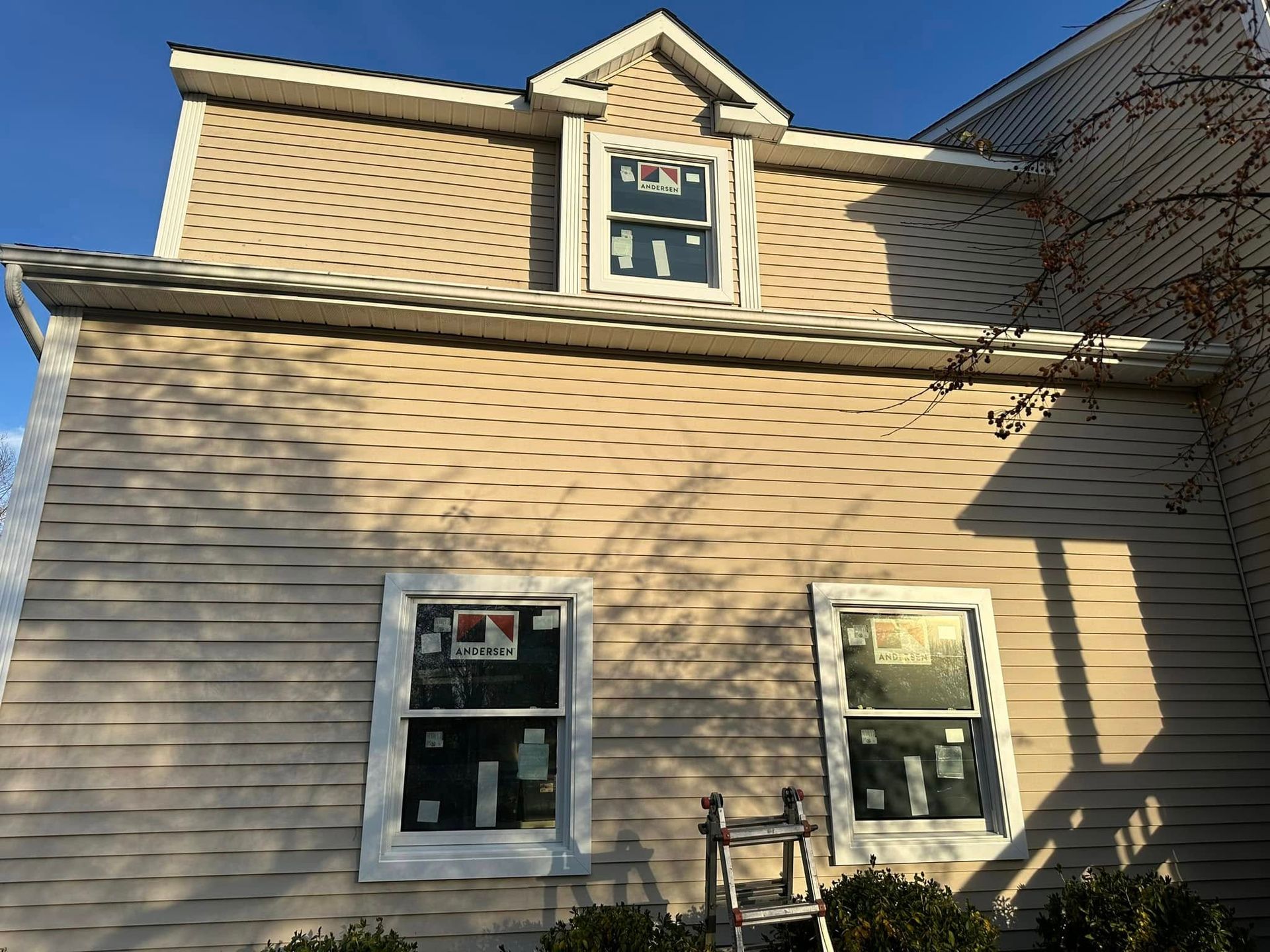 Tan house with three windows; ladder rests against the wall. Sunny day.