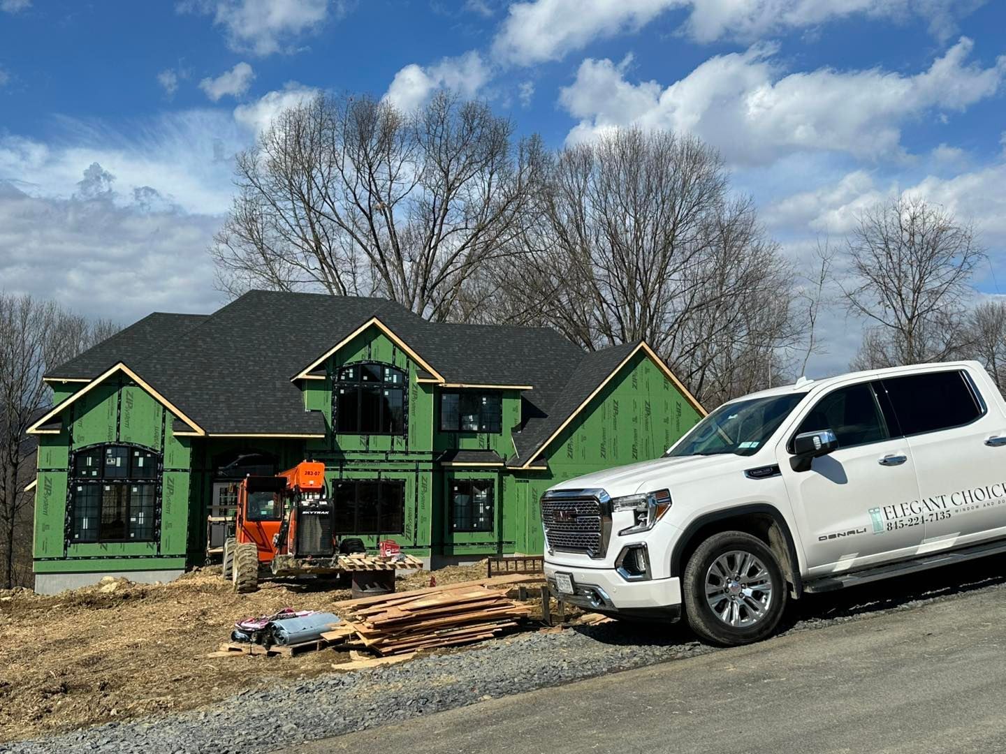 White truck parked near a house under construction; green siding, black roof, small excavator visible.