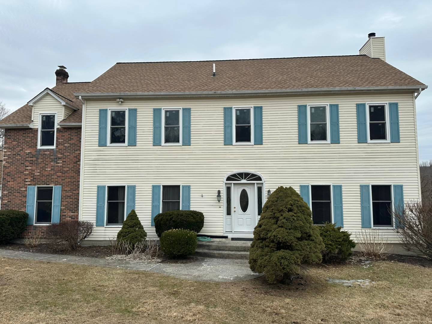 Two-story beige house with blue shutters, a brown roof, and a brick accent.