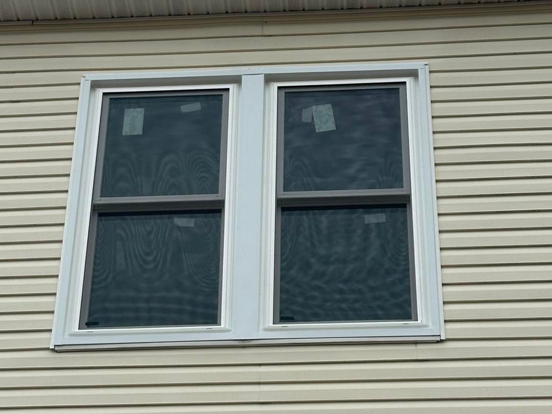 White-framed double-hung window with dark screens against tan siding.