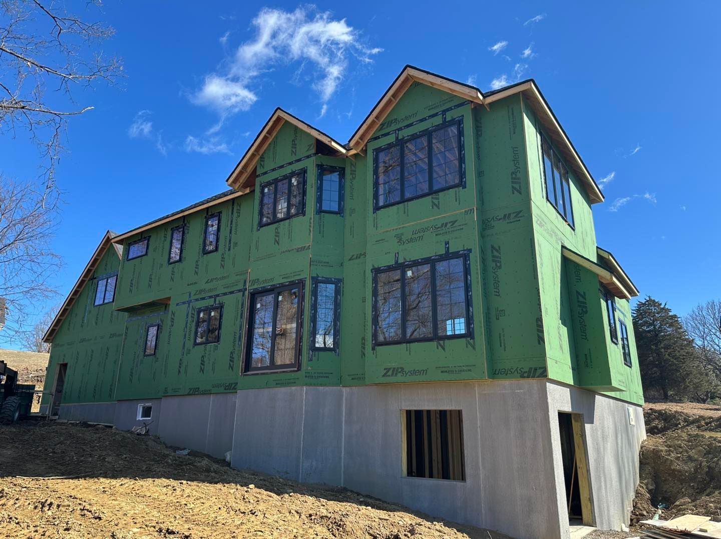 New house under construction with green wrap and dark window frames against a blue sky.