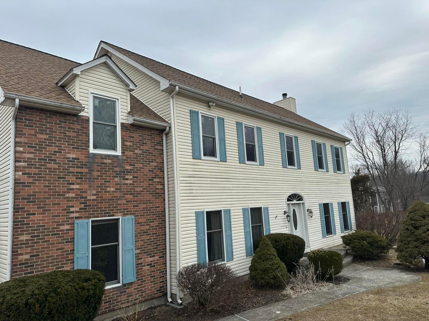 Two-story house with brick and beige siding, blue shutters, and brown roof.
