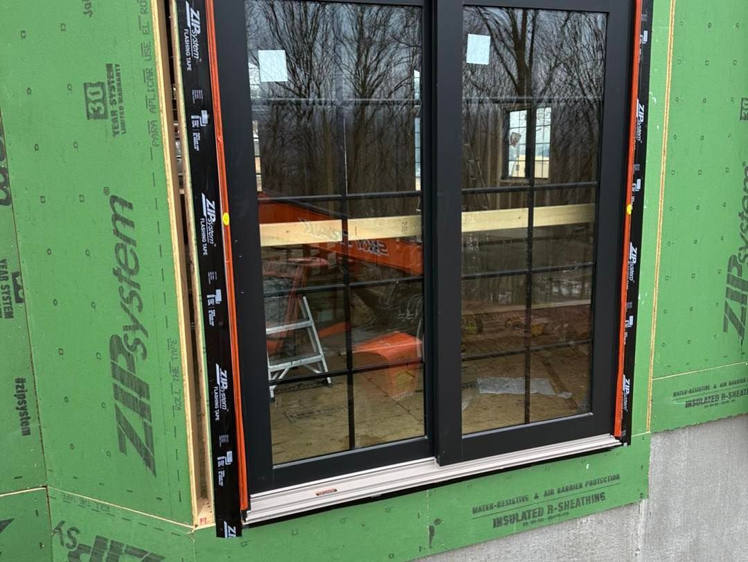 Black framed window installed in a new construction opening, sealed with black flashing tape.