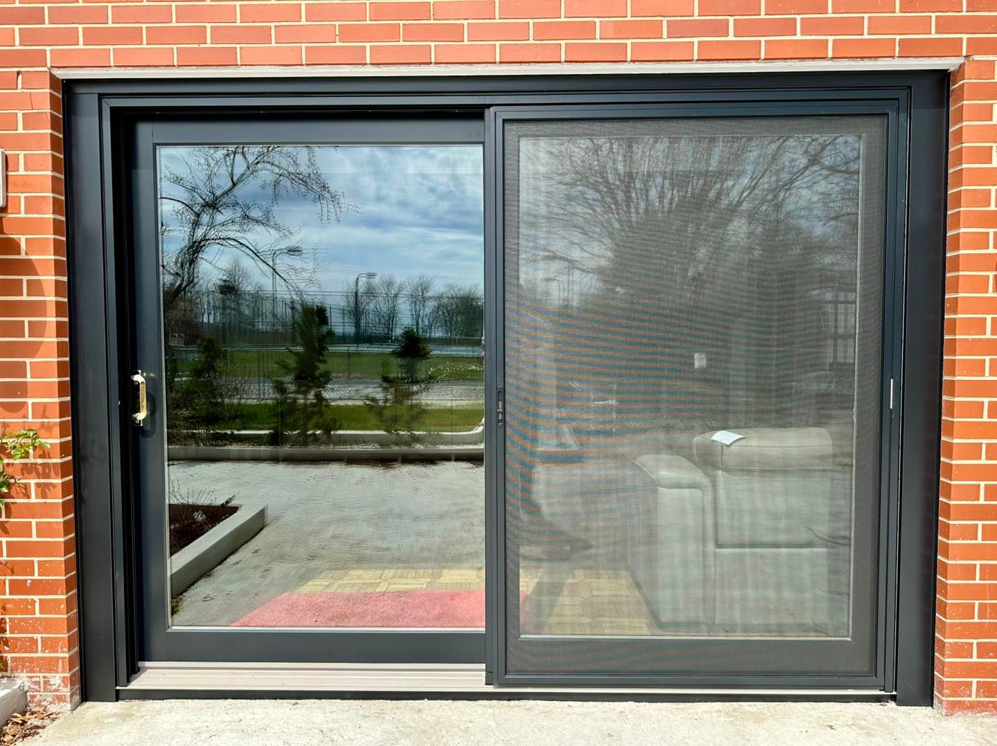 Sliding glass door with screen, dark frame, set in brick wall, reflecting outdoors.