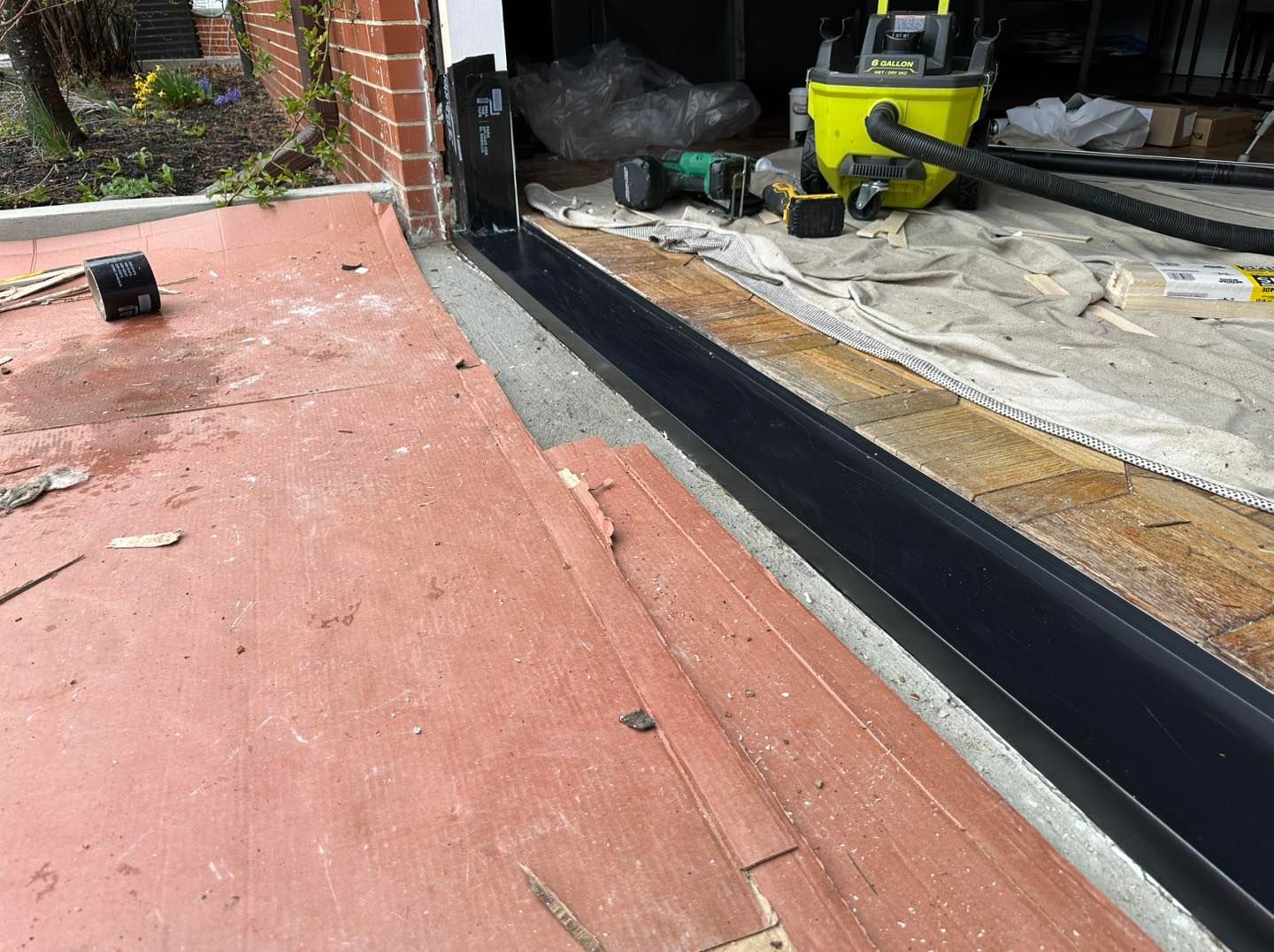 Construction site, red concrete, black metal frame, power tools, doorway, and plywood.