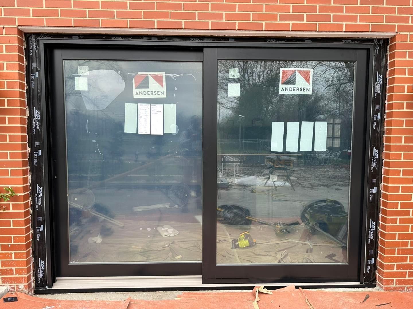 Black sliding glass door installed in a red brick wall, covered in protective film.