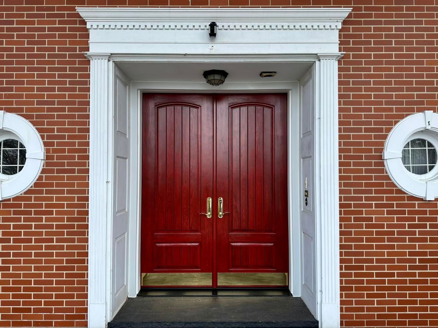 Red double doors with gold hardware and white trim in a brick building.