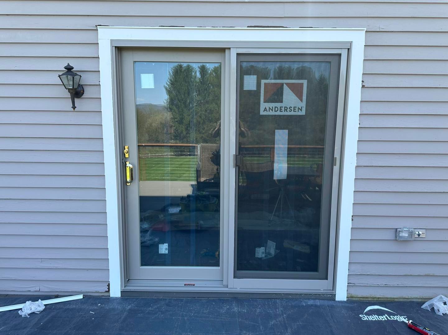 Sliding glass door, beige frame, gray siding, exterior view.
