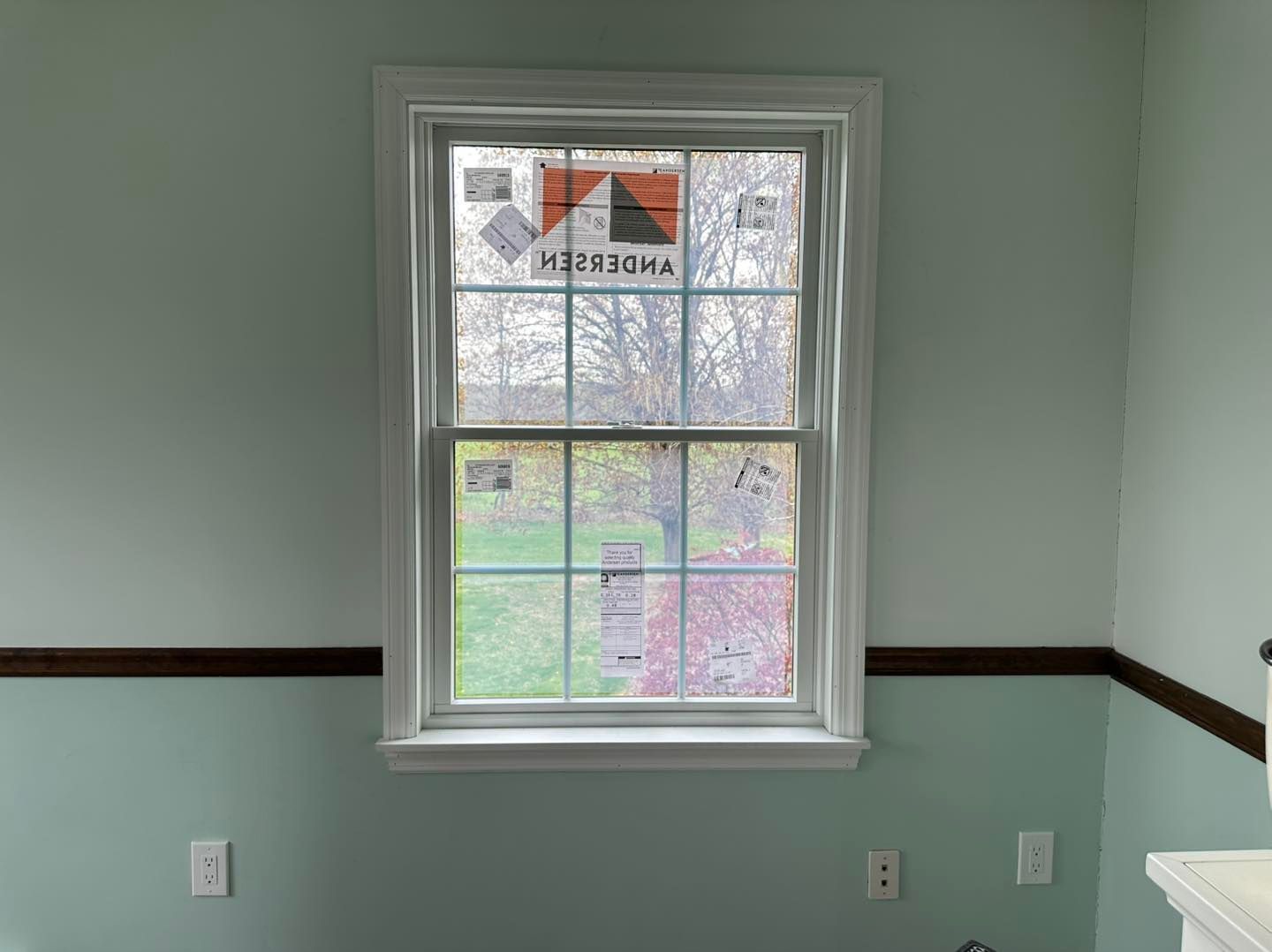 A window with white trim in a room with light green walls and brown trim.