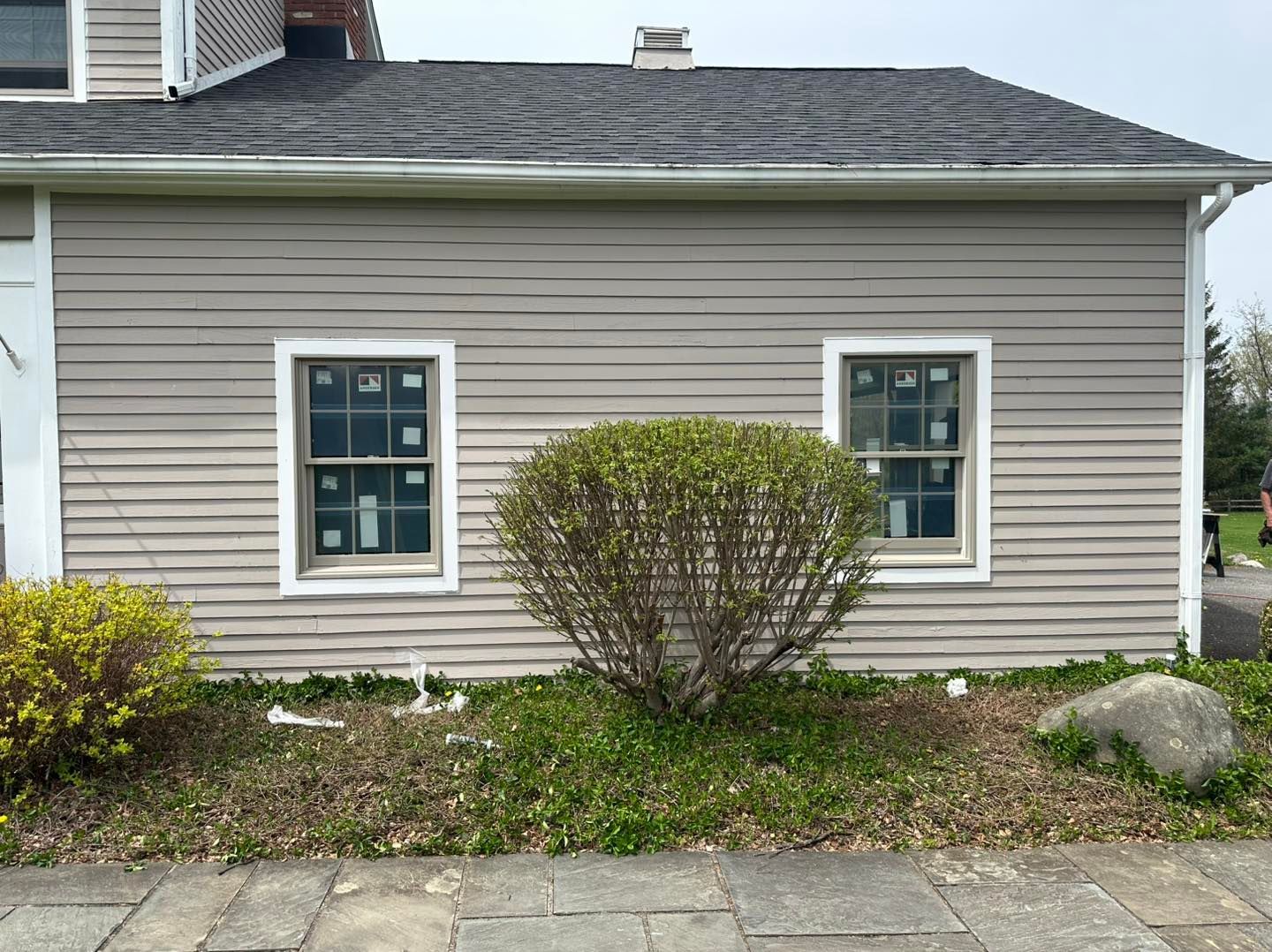 Exterior of a light gray house with two windows and a bush in front.
