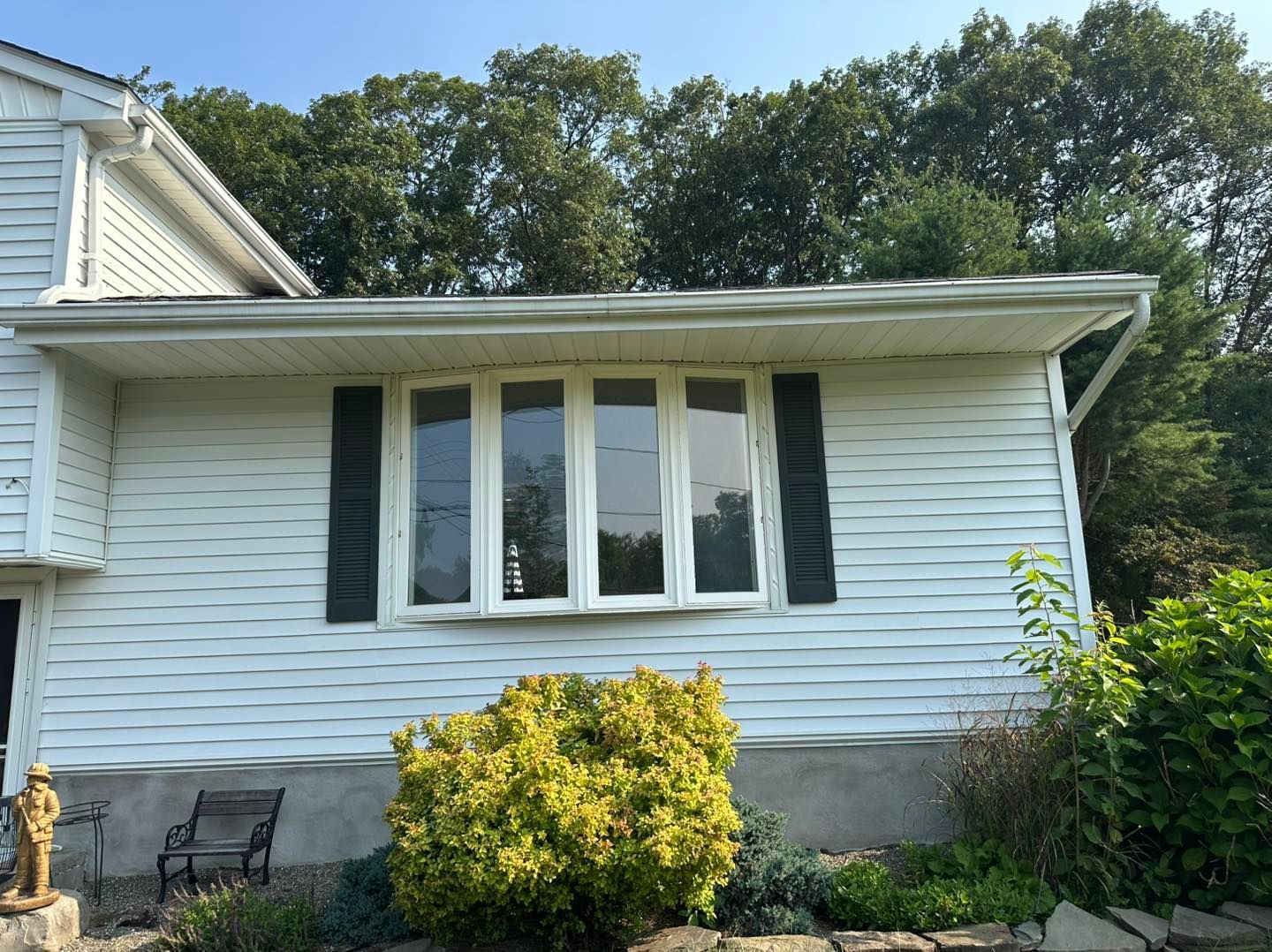 White house with bay window, black shutters, and bushes in front.