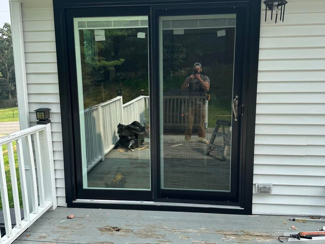 Black framed sliding glass door on a white house, person reflected.