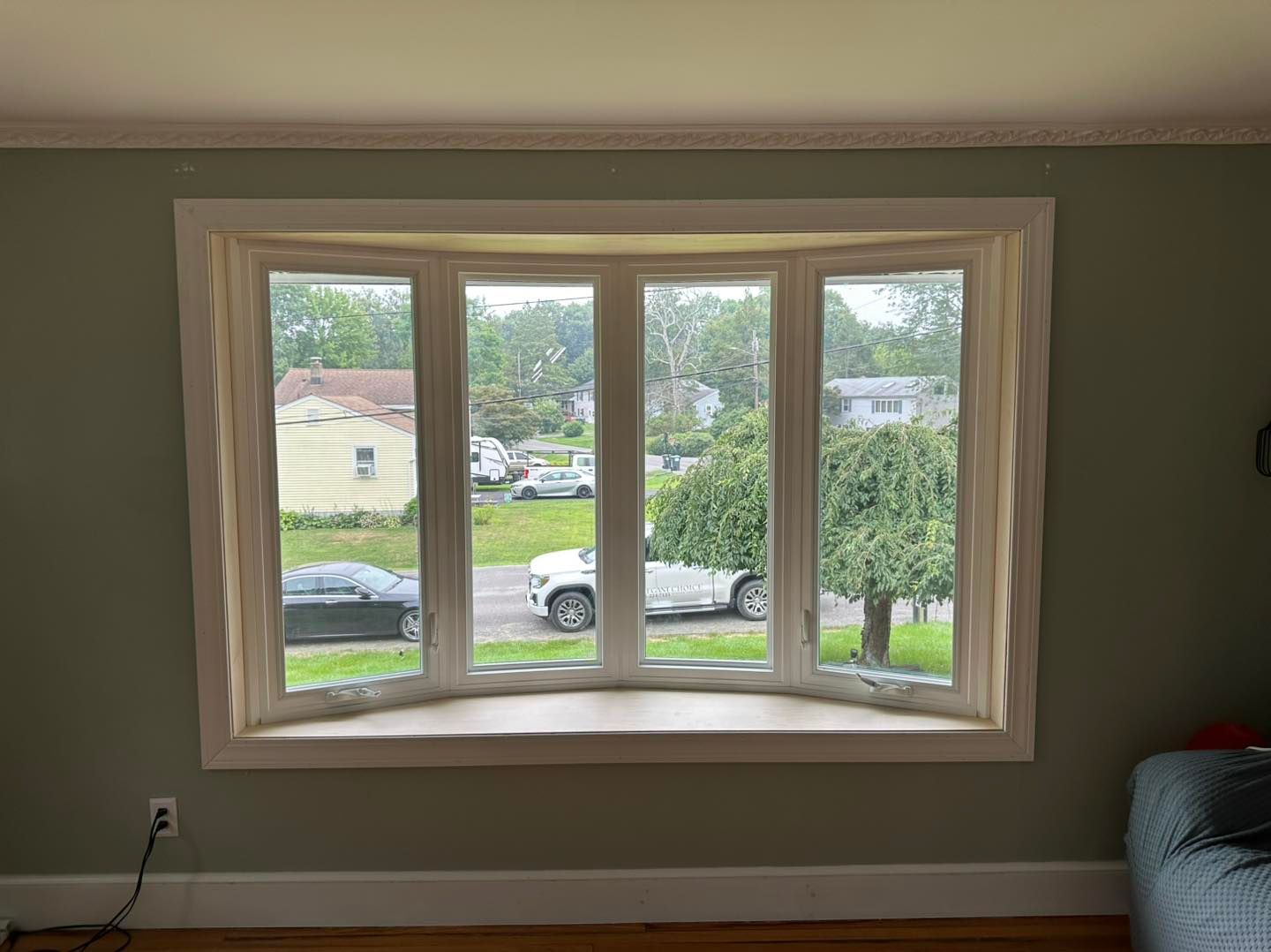 Bay window with white trim in a room with green walls, overlooking a street with vehicles and trees.