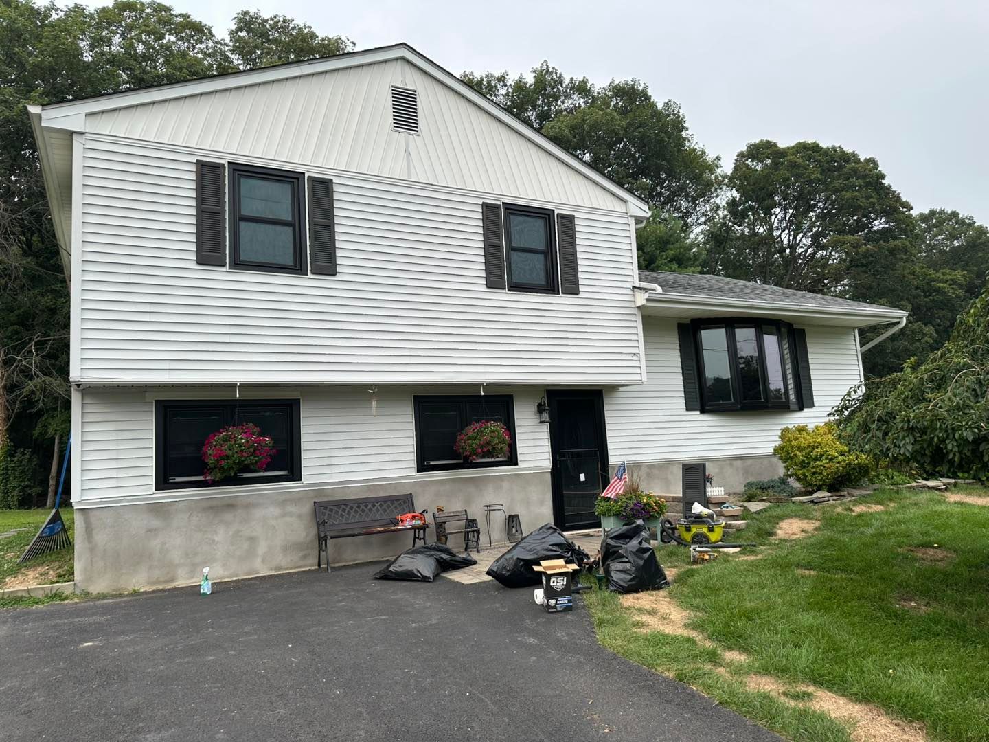 White house with black shutters, windows, and door. Landscaping and driveway in front.