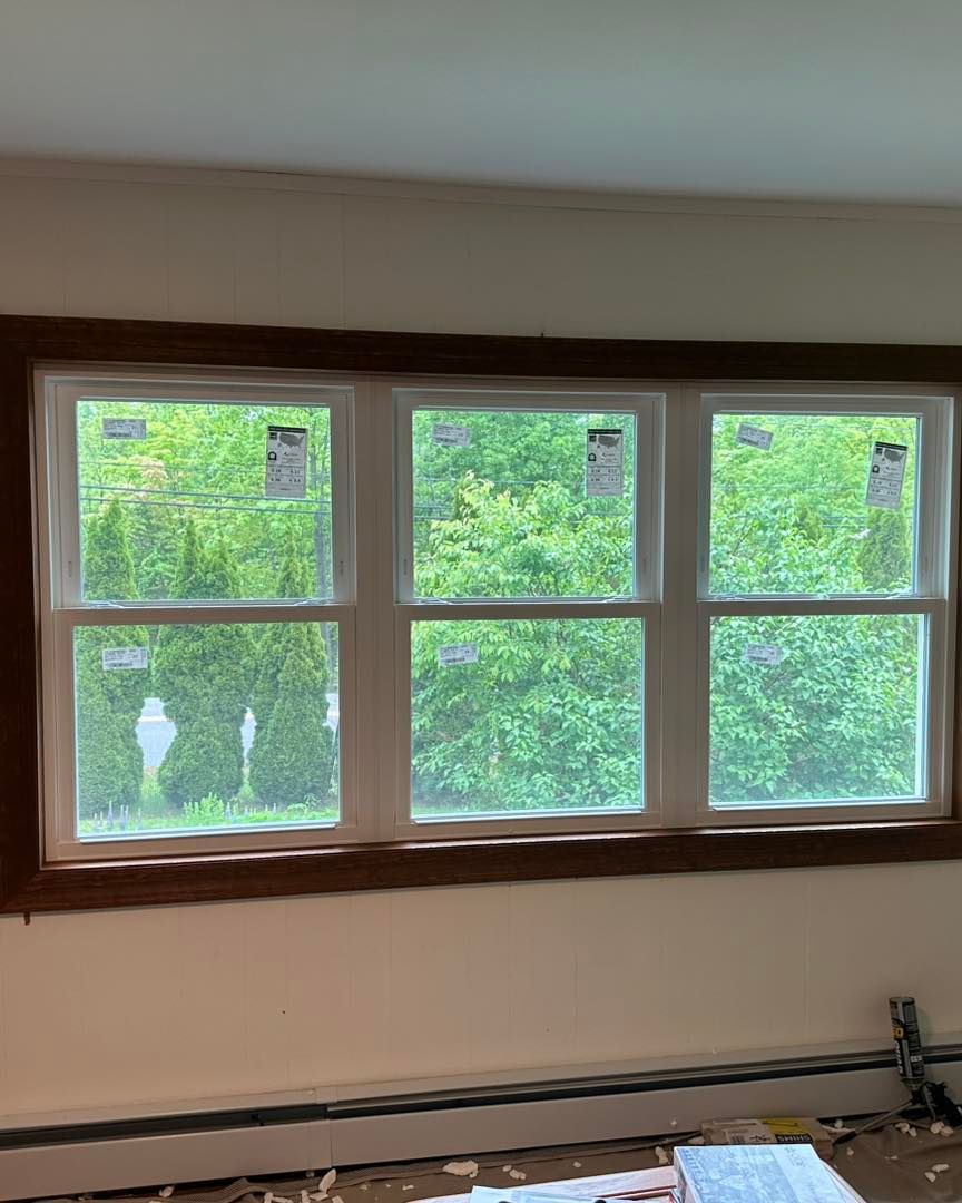 Triple-pane window with white frames and brown trim, overlooking a green, leafy landscape.