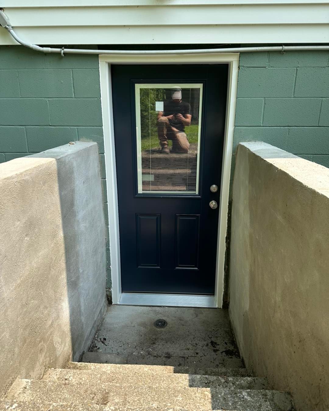 Exterior door with a window set in a concrete stairwell, painted navy blue, leading into a building.