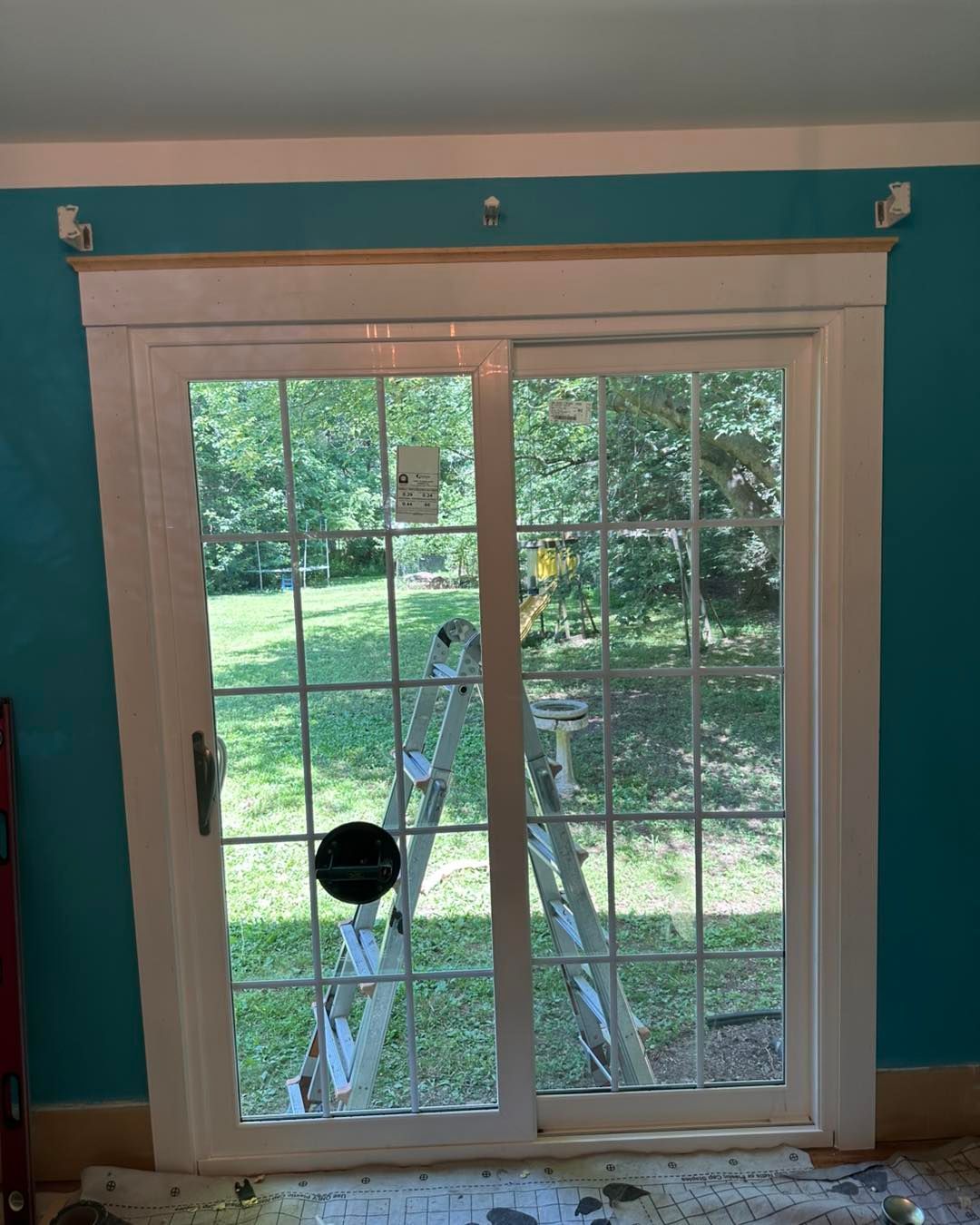 Sliding glass door with white trim, unfinished wood header, turquoise walls. Ladder inside.